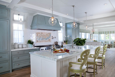 This is an example of a beach style galley open plan kitchen in San Diego with shaker cabinets, marble benchtops, white splashback, subway tile splashback, stainless steel appliances, with island, a farmhouse sink, medium hardwood floors and blue cabinets.