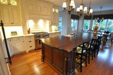 Inspiration for a mid-sized transitional l-shaped medium tone wood floor open concept kitchen remodel in Other with a farmhouse sink, beaded inset cabinets, white cabinets, granite countertops, white backsplash, stone tile backsplash, paneled appliances and an island