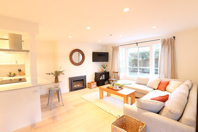 This is an example of a small contemporary formal enclosed living room in Vancouver with white walls, light hardwood floors, a standard fireplace, a plaster fireplace surround, a wall-mounted tv and brown floor.