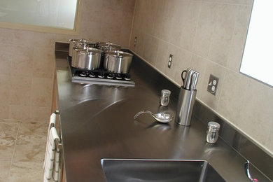 Example of a large l-shaped enclosed kitchen design in Toronto with an integrated sink, stainless steel countertops, stainless steel appliances and an island