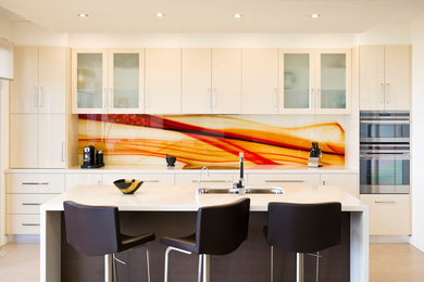 Design ideas for a mid-sized contemporary l-shaped eat-in kitchen in Melbourne with a double-bowl sink, flat-panel cabinets, grey cabinets, solid surface benchtops, multi-coloured splashback, glass sheet splashback, black appliances, ceramic floors, with island, beige floor and white benchtop.