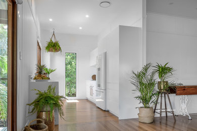 Small modern galley open plan kitchen in Gold Coast - Tweed with a drop-in sink, flat-panel cabinets, white cabinets, quartz benchtops, white splashback, stone slab splashback, white appliances, light hardwood floors, no island, brown floor and white benchtop.