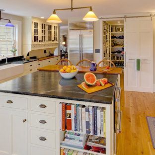 Large farmhouse kitchen pantry designs - Example of a large cottage u-shaped light wood floor kitchen pantry design in Portland Maine with a farmhouse sink, white cabinets, white backsplash, ceramic backsplash, stainless steel appliances, an island, shaker cabinets and soapstone countertops