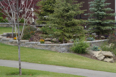 This is an example of a large traditional partial sun front yard mulch retaining wall landscape in Calgary.