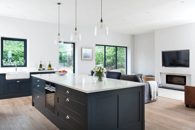 Design ideas for a mid-sized country single-wall eat-in kitchen in Belfast with a farmhouse sink, shaker cabinets, grey cabinets, quartzite benchtops, metallic splashback, glass sheet splashback, stainless steel appliances, medium hardwood floors and with island.