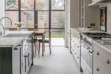 This is an example of a large modern grey and white single-wall kitchen/diner in London with a belfast sink, shaker cabinets, grey cabinets, composite countertops, white splashback, marble splashback, stainless steel appliances, porcelain flooring, an island, beige floors and white worktops.