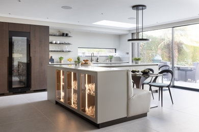 Inspiration for a large contemporary l-shaped kitchen/diner in Hertfordshire with flat-panel cabinets, grey cabinets, quartz worktops, grey splashback, black appliances, ceramic flooring, an island, grey floors, beige worktops and feature lighting.