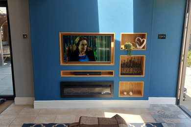 This is an example of a medium sized modern open plan living room feature wall in Surrey with blue walls, porcelain flooring, a standard fireplace, a metal fireplace surround, a built-in media unit, multi-coloured floors, a vaulted ceiling and wood walls.