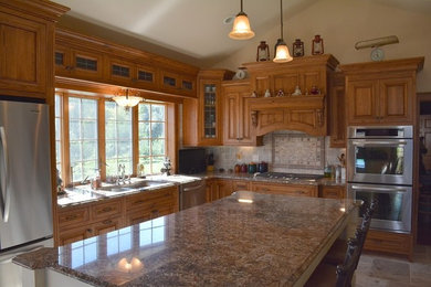 Open concept kitchen - mid-sized traditional l-shaped ceramic tile open concept kitchen idea in Milwaukee with a double-bowl sink, medium tone wood cabinets, granite countertops, beige backsplash, porcelain backsplash, stainless steel appliances, an island and raised-panel cabinets