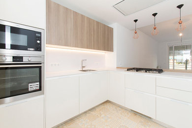 Inspiration for a mid-sized contemporary l-shaped open plan kitchen in Barcelona with a single-bowl sink, flat-panel cabinets, stainless steel appliances, a peninsula and white cabinets.