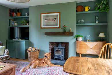 This is an example of a small rural living room in London with green walls, a wood burning stove and panelled walls.