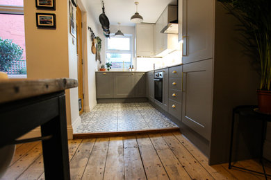 Photo of a small rustic grey and white l-shaped open plan kitchen in Other with a submerged sink, shaker cabinets, grey cabinets, integrated appliances, ceramic flooring, no island, multi-coloured floors, white worktops and feature lighting.