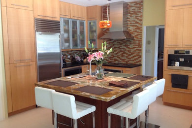 This is an example of a large contemporary u-shaped kitchen in Miami with an undermount sink, flat-panel cabinets, medium wood cabinets, granite benchtops, multi-coloured splashback, glass sheet splashback, stainless steel appliances, limestone floors and with island.