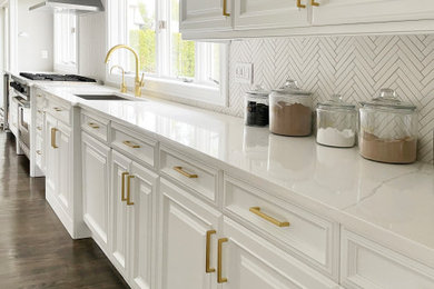 Example of a transitional dark wood floor and brown floor kitchen design in New York with an undermount sink, raised-panel cabinets, white cabinets, quartz countertops, white backsplash, porcelain backsplash, stainless steel appliances and white countertops