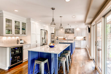 Design ideas for a large transitional l-shaped eat-in kitchen in Denver with a farmhouse sink, shaker cabinets, blue cabinets, white splashback, subway tile splashback, stainless steel appliances and multiple islands.