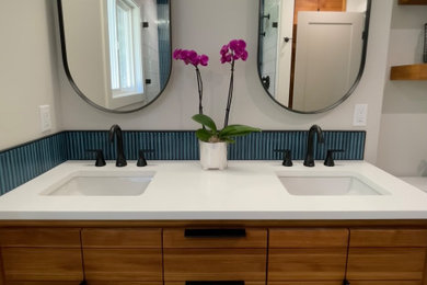 Example of a mid-sized transitional blue tile and porcelain tile porcelain tile, gray floor and double-sink shower bench design in Portland with flat-panel cabinets, medium tone wood cabinets, a two-piece toilet, gray walls, an undermount sink, solid surface countertops, a hinged shower door, white countertops and a freestanding vanity
