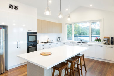 Inspiration for a mid-sized contemporary l-shaped open plan kitchen in Melbourne with a double-bowl sink, white cabinets, quartz benchtops, white splashback, ceramic splashback, black appliances, dark hardwood floors, with island, brown floor, white benchtop and vaulted.