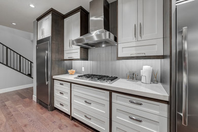 Example of a minimalist light wood floor kitchen design in Calgary with recessed-panel cabinets, white cabinets and stainless steel appliances