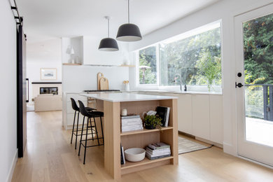Inspiration for a scandinavian l-shaped light wood floor and brown floor eat-in kitchen remodel in Vancouver with flat-panel cabinets, white cabinets, white backsplash, stainless steel appliances, an island and white countertops