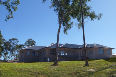Photo of a large transitional one-storey brick grey house exterior in Brisbane with a hip roof and a metal roof.