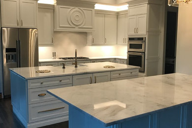 Large minimalist dark wood floor and brown floor eat-in kitchen photo in St Louis with a farmhouse sink, recessed-panel cabinets, white cabinets, marble countertops, stainless steel appliances and two islands