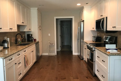 Eat-in kitchen - mid-sized traditional galley medium tone wood floor and brown floor eat-in kitchen idea in Other with a double-bowl sink, recessed-panel cabinets, white cabinets, granite countertops, multicolored backsplash, travertine backsplash and stainless steel appliances