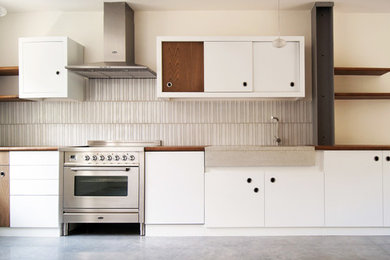 Cette photo montre une cuisine ouverte linéaire scandinave de taille moyenne avec des portes de placard blanches, un plan de travail en bois, une crédence grise et une crédence en céramique.