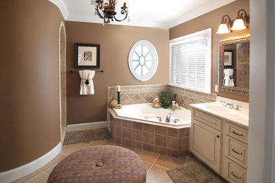 Photo of a large traditional master bathroom in Raleigh with white cabinets, a corner tub, beige tile, brown tile, beige walls, raised-panel cabinets, porcelain tile, porcelain floors, an integrated sink, engineered quartz benchtops and beige floor.