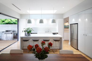 Large contemporary l-shaped open plan kitchen in Sydney with an undermount sink, flat-panel cabinets, white cabinets, quartz benchtops, white splashback, stone slab splashback, stainless steel appliances, medium hardwood floors, with island and brown floor.