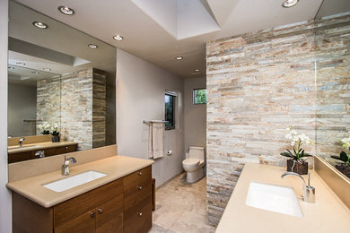 Design ideas for a mid-sized contemporary master bathroom in Phoenix with a one-piece toilet, grey walls, ceramic floors, an undermount sink, beige floor, a corner shower, a hinged shower door, flat-panel cabinets, medium wood cabinets, beige tile, brown tile, stone tile and granite benchtops.