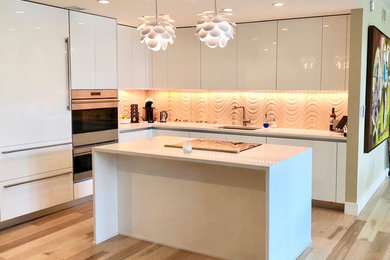 Example of a mid-sized trendy l-shaped light wood floor and beige floor open concept kitchen design in DC Metro with an undermount sink, flat-panel cabinets, white cabinets, solid surface countertops, white backsplash, porcelain backsplash, paneled appliances, an island and white countertops