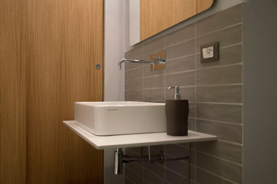 Idee per una stanza da bagno con doccia design di medie dimensioni con doccia doppia, WC sospeso, piastrelle grigie, piastrelle in gres porcellanato, pareti grigie, pavimento in gres porcellanato, lavabo a bacinella, top in superficie solida, pavimento grigio, doccia aperta e top grigio