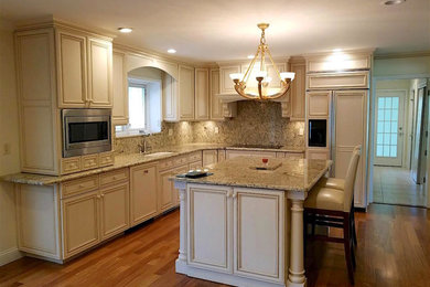 This is an example of a mid-sized transitional l-shaped open plan kitchen in New York with an undermount sink, recessed-panel cabinets, white cabinets, granite benchtops, beige splashback, stone slab splashback, stainless steel appliances, medium hardwood floors, with island and brown floor.