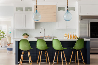 Inspiration for a large beach style l-shaped eat-in kitchen in Boston with a single-bowl sink, shaker cabinets, white cabinets, granite benchtops, white splashback, glass tile splashback, stainless steel appliances, light hardwood floors, with island, white floor and white benchtop.