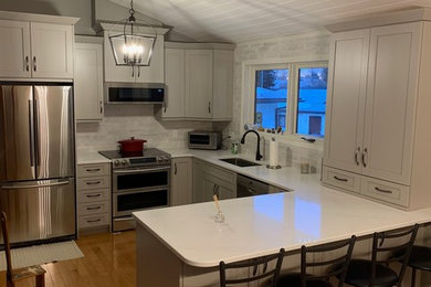 Photo of a small transitional u-shaped eat-in kitchen in Edmonton with an undermount sink, shaker cabinets, grey cabinets, quartz benchtops, grey splashback, ceramic splashback, stainless steel appliances, medium hardwood floors, a peninsula, brown floor and white benchtop.
