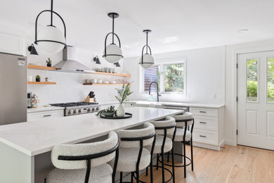 Mid-sized trendy light wood floor eat-in kitchen photo in Burlington with a farmhouse sink, shaker cabinets, white cabinets, quartz countertops, white backsplash, mosaic tile backsplash, stainless steel appliances and an island