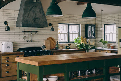 Country l-shaped kitchen in London with a farmhouse sink, open cabinets, green cabinets, wood benchtops, white splashback, subway tile splashback, with island and grey floor.