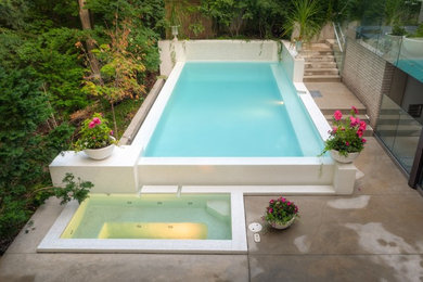 Small modern backyard rectangular infinity pool in Toronto with a hot tub and stamped concrete.