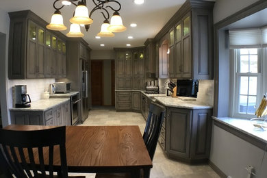 Inspiration for a mid-sized traditional kitchen in Cleveland with a farmhouse sink, raised-panel cabinets, grey cabinets, quartz benchtops, white splashback, subway tile splashback, stainless steel appliances, vinyl floors and multi-coloured floor.