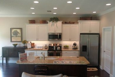 Example of a mid-sized classic single-wall dark wood floor and brown floor open concept kitchen design in Orlando with an undermount sink, recessed-panel cabinets, white cabinets, granite countertops, white backsplash, ceramic backsplash, stainless steel appliances and an island