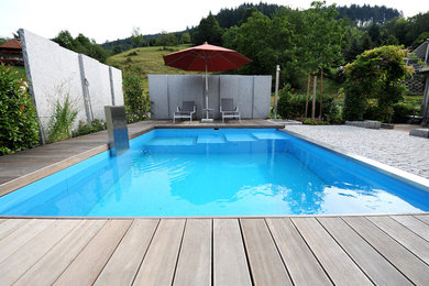 Large contemporary backyard rectangular lap pool in Other with decking and a water feature.