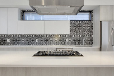 Example of a minimalist single-wall kitchen design in Calgary with flat-panel cabinets, white cabinets, quartz countertops, black backsplash, cement tile backsplash, an island, an undermount sink and stainless steel appliances