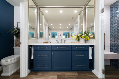 Example of a transitional master porcelain tile, brown floor and double-sink bathroom design in Orange County with shaker cabinets, blue cabinets, white walls, an undermount sink, quartz countertops, a hinged shower door, white countertops and a built-in vanity
