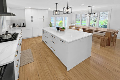 Photo of a large modern u-shaped eat-in kitchen in Philadelphia with a farmhouse sink, flat-panel cabinets, white cabinets, quartz benchtops, grey splashback, porcelain splashback, black appliances, bamboo floors, with island, brown floor and white benchtop.