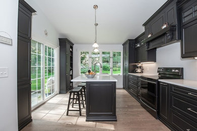 Kitchen - large traditional single-wall light wood floor and beige floor kitchen idea in New York with a farmhouse sink, raised-panel cabinets, black cabinets, solid surface countertops, white backsplash, stainless steel appliances, an island and white countertops