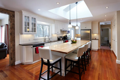 Inspiration for a cottage l-shaped kitchen pantry remodel in Toronto with a drop-in sink, recessed-panel cabinets, white cabinets, wood countertops, white backsplash and stainless steel appliances