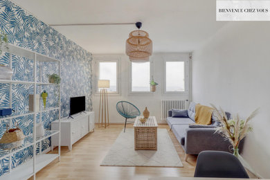 Modelo de salón tropical de tamaño medio con paredes azules, suelo laminado, televisor independiente, suelo beige y papel pintado