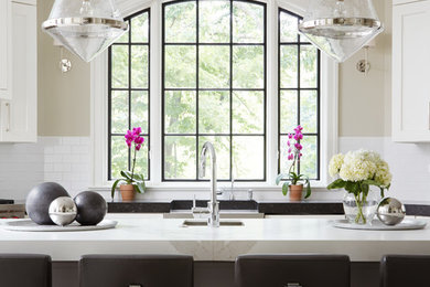 Inspiration for a large transitional u-shaped eat-in kitchen remodel in Chicago with a farmhouse sink, shaker cabinets, white cabinets, white backsplash, subway tile backsplash, an island, solid surface countertops and stainless steel appliances