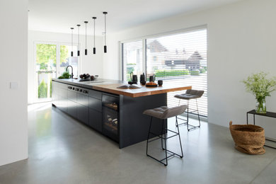 Moderne Küche mit flächenbündigen Schrankfronten, schwarzen Schränken, Granit-Arbeitsplatte, schwarzen Elektrogeräten, Betonboden, Kücheninsel, grauem Boden und grauer Arbeitsplatte in München