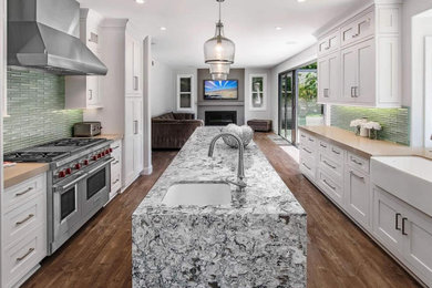 Example of a transitional galley dark wood floor and brown floor eat-in kitchen design in Other with a farmhouse sink, shaker cabinets, white cabinets, quartz countertops, green backsplash, mosaic tile backsplash, stainless steel appliances and an island